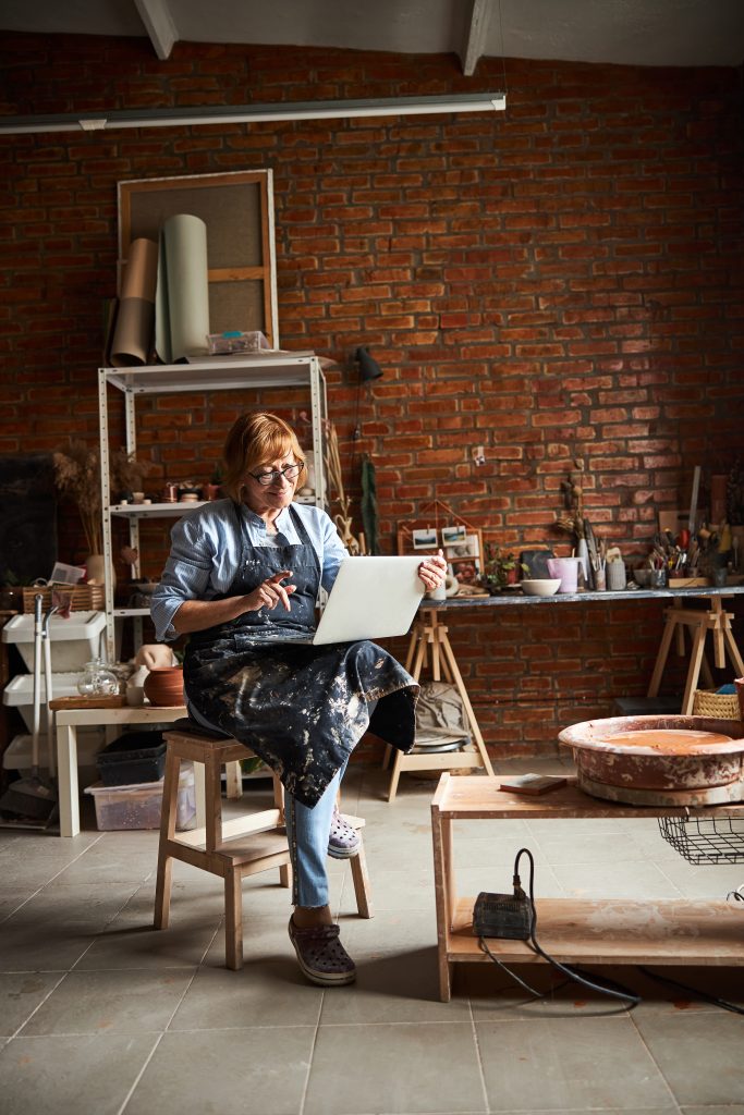 Nice female potter using notebook in pottery workshop